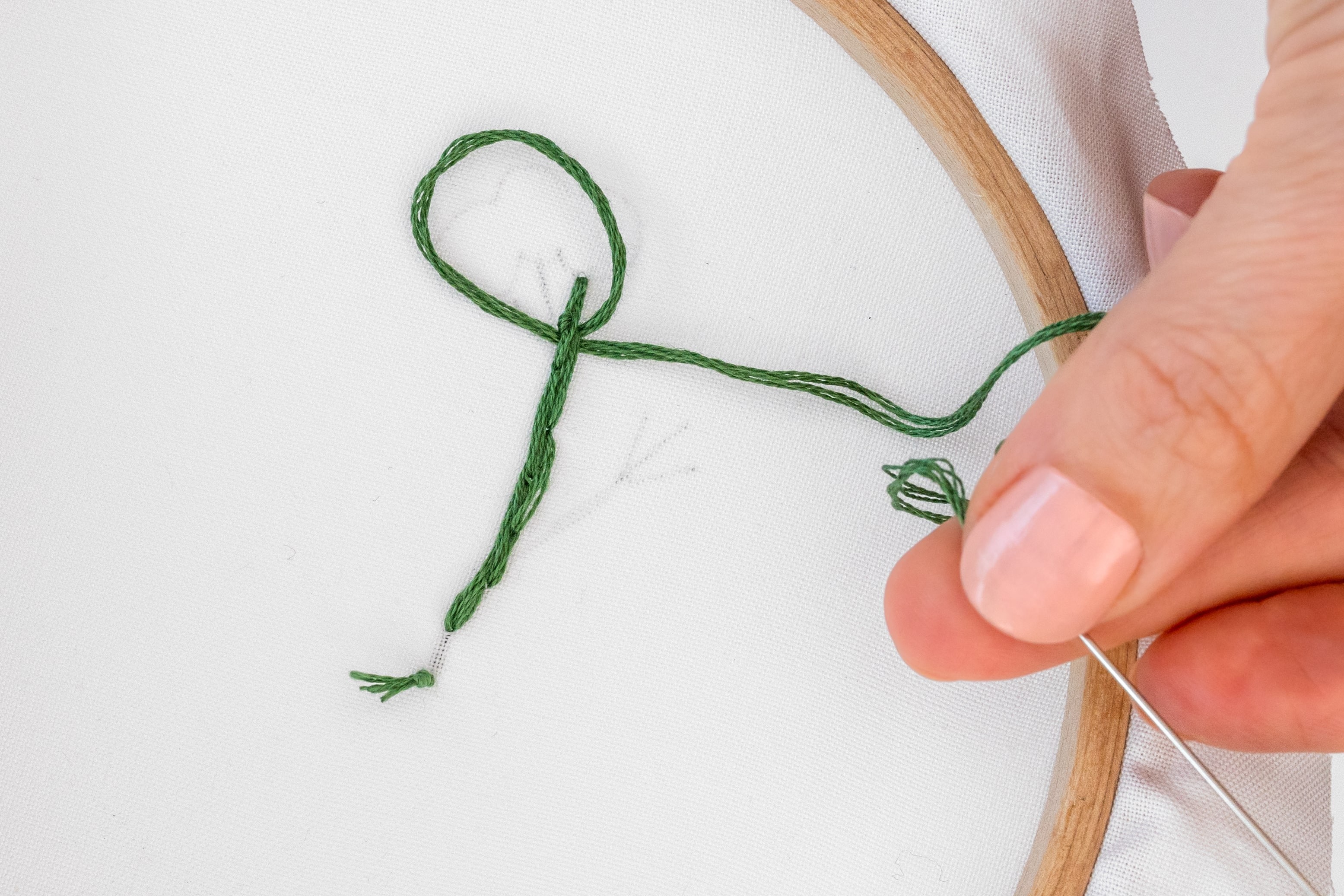 A hand creates a loop at the back of some stitching.