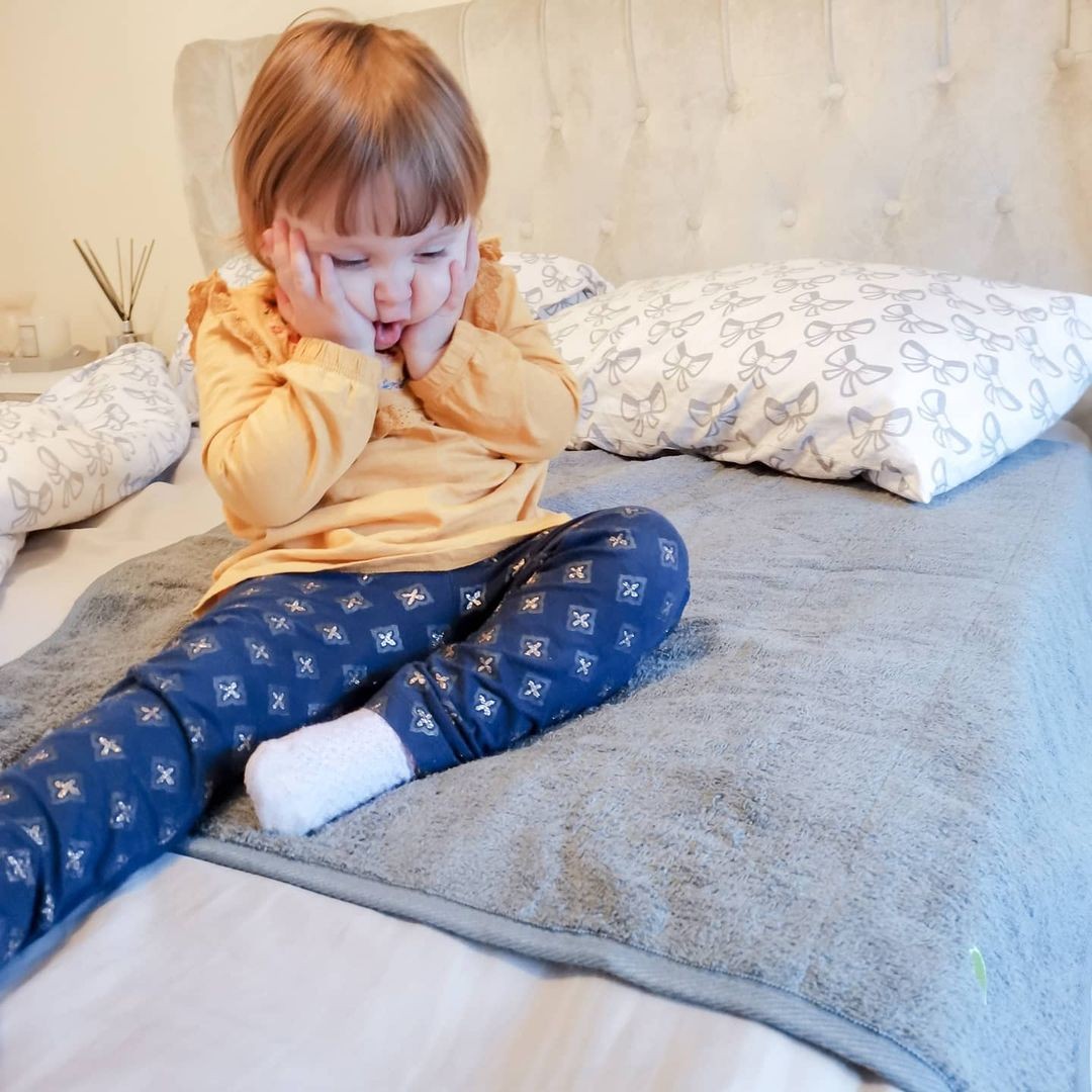little girl sitting on the bed with PeapodMat