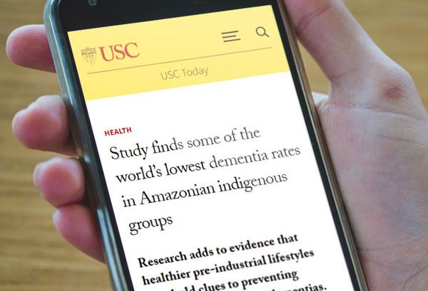 Person scrolling on a smartphone displaying a USC news article titled “Study finds some of the world’s lowest dementia rates in Amazonian indigenous groups.”