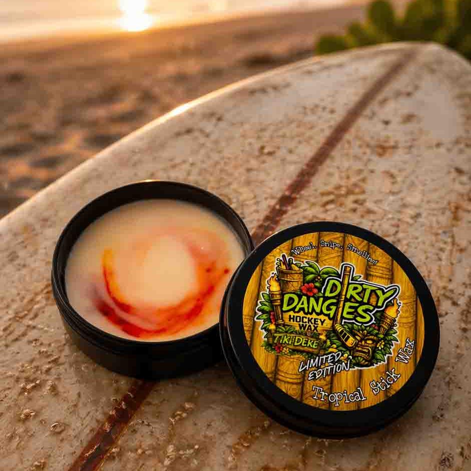An open tin of dirty dangles tiki deke limited edition tropical stick wax on a rustic surfboard at the beach
