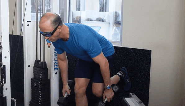 Man In Blue with Shorts Holding Dumbbells in Gym Outside View