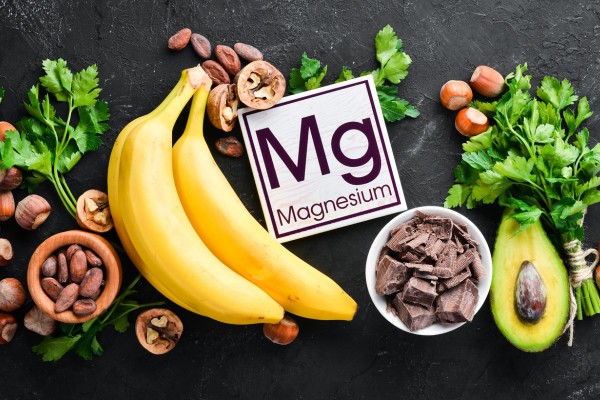 a wooden block with the word "magnesium" on it surrounded by various magnesium-rich foods (bananas, nuts, chocolate, avocado)