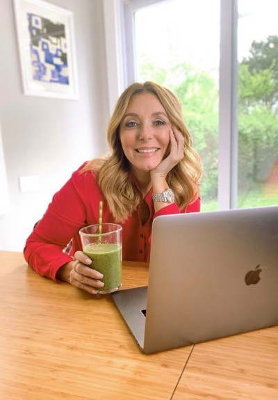 Dr. Kellyann sitting in front of MacBook with a green smoothie