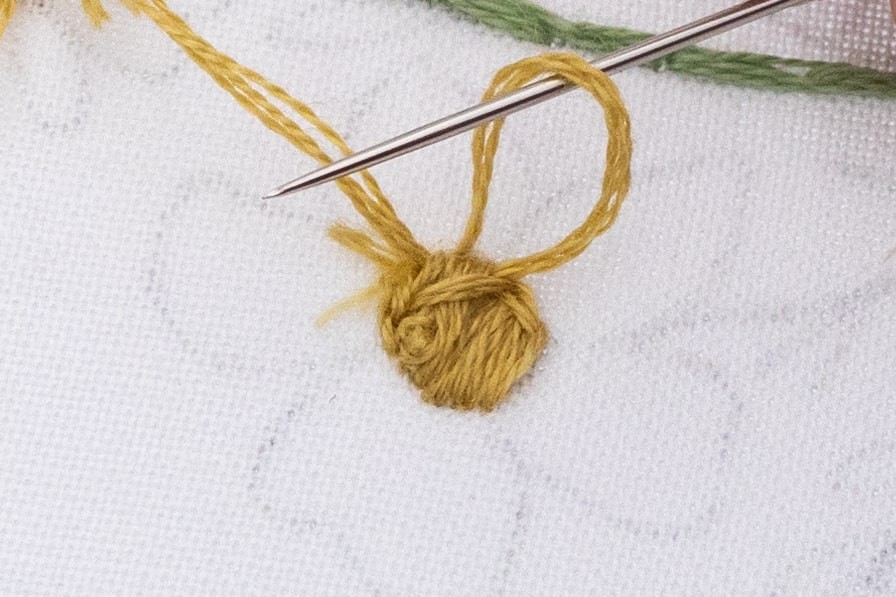 A needle is being pulled through a loop in satin stitch.