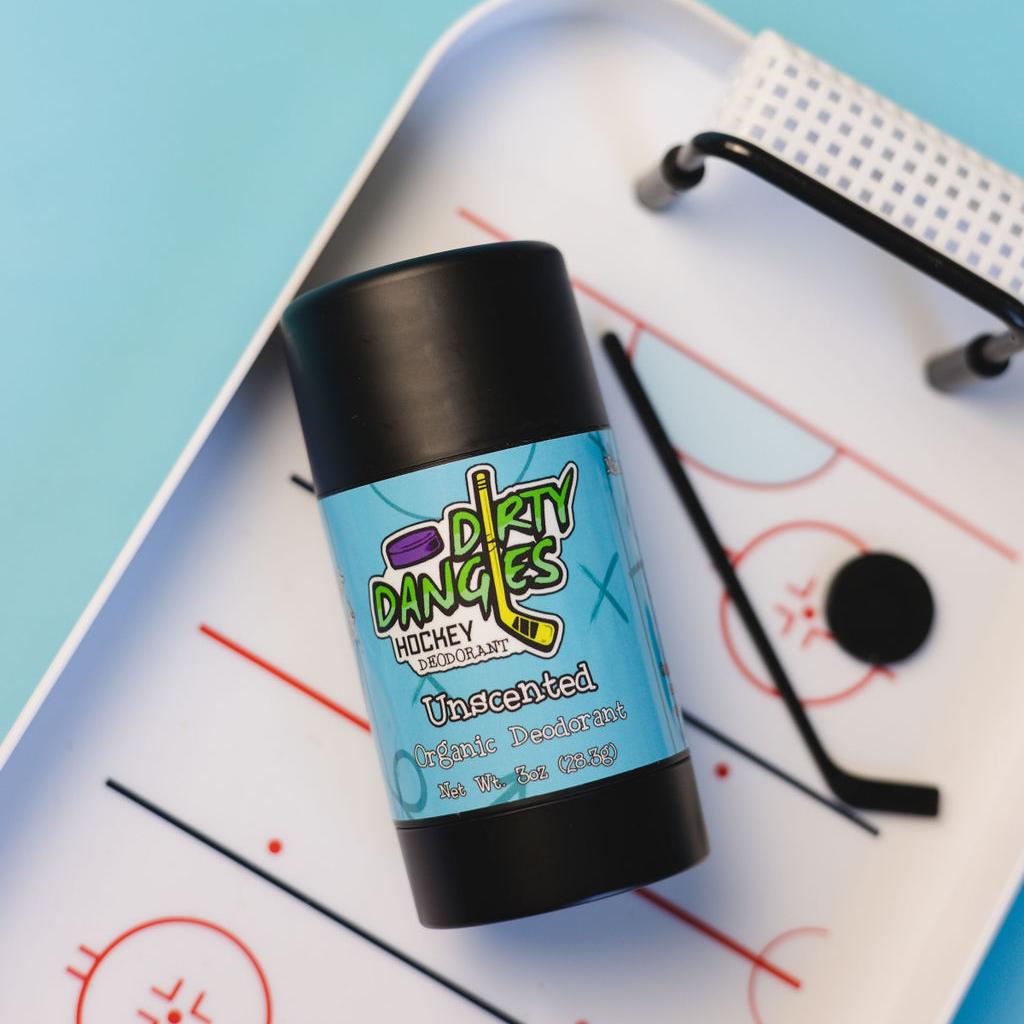 A tube of dirty dangles fragrance free aluminum-free unscented natural hockey deodorant on a blue background with hockey toys