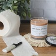 A beige candle sitting on a wood table with a roll of toilet paper and a lighter. Butt sweat and tears