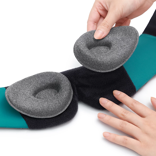 The interior of a weighted eye mask for insomnia is laid out flat. A hand is holding one of the detachable tapered eye cups.