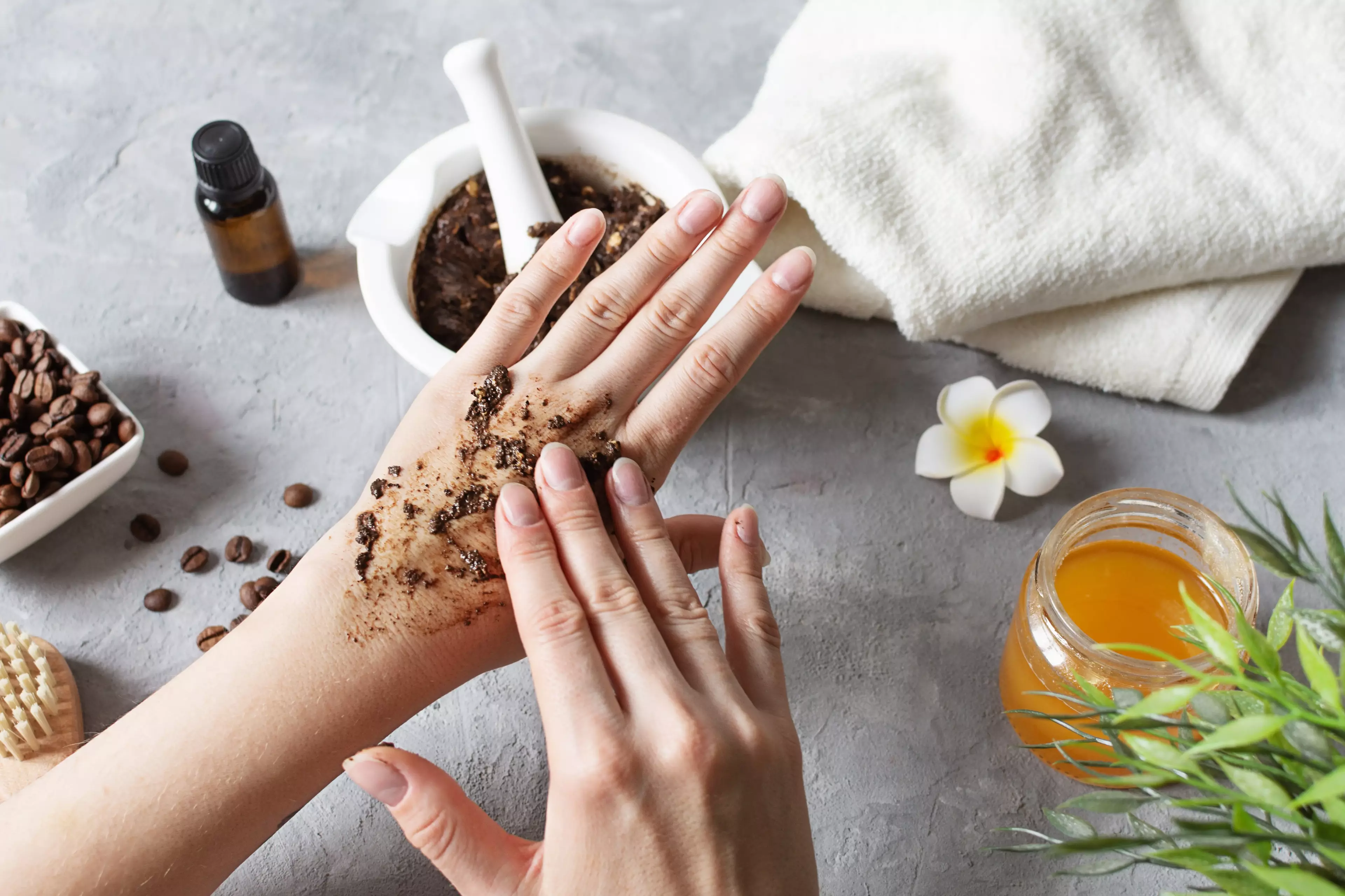 Coffee grounds scrub being massaged onto a hand on a spa-style counter with towel, honey and coffee beans.