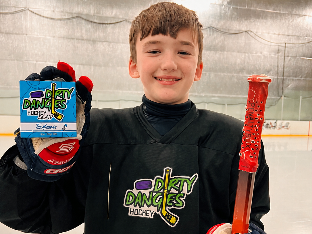 Youth hockey player on the ice holding The Michigan sea salt hockey soap bar and a hockey stick.