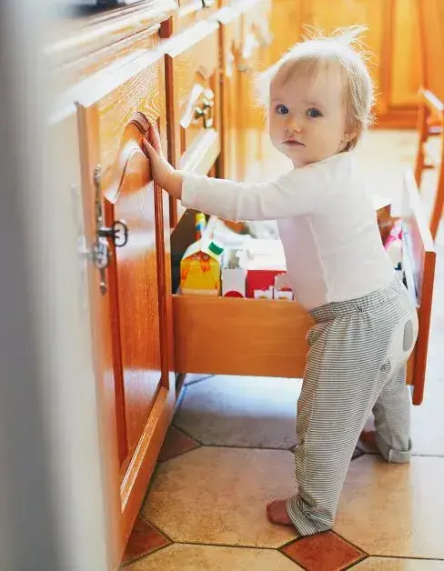 A toddler stands in a kitchen drawer, illustrating tips on preventing toddlers from accessing kitchen drawers.