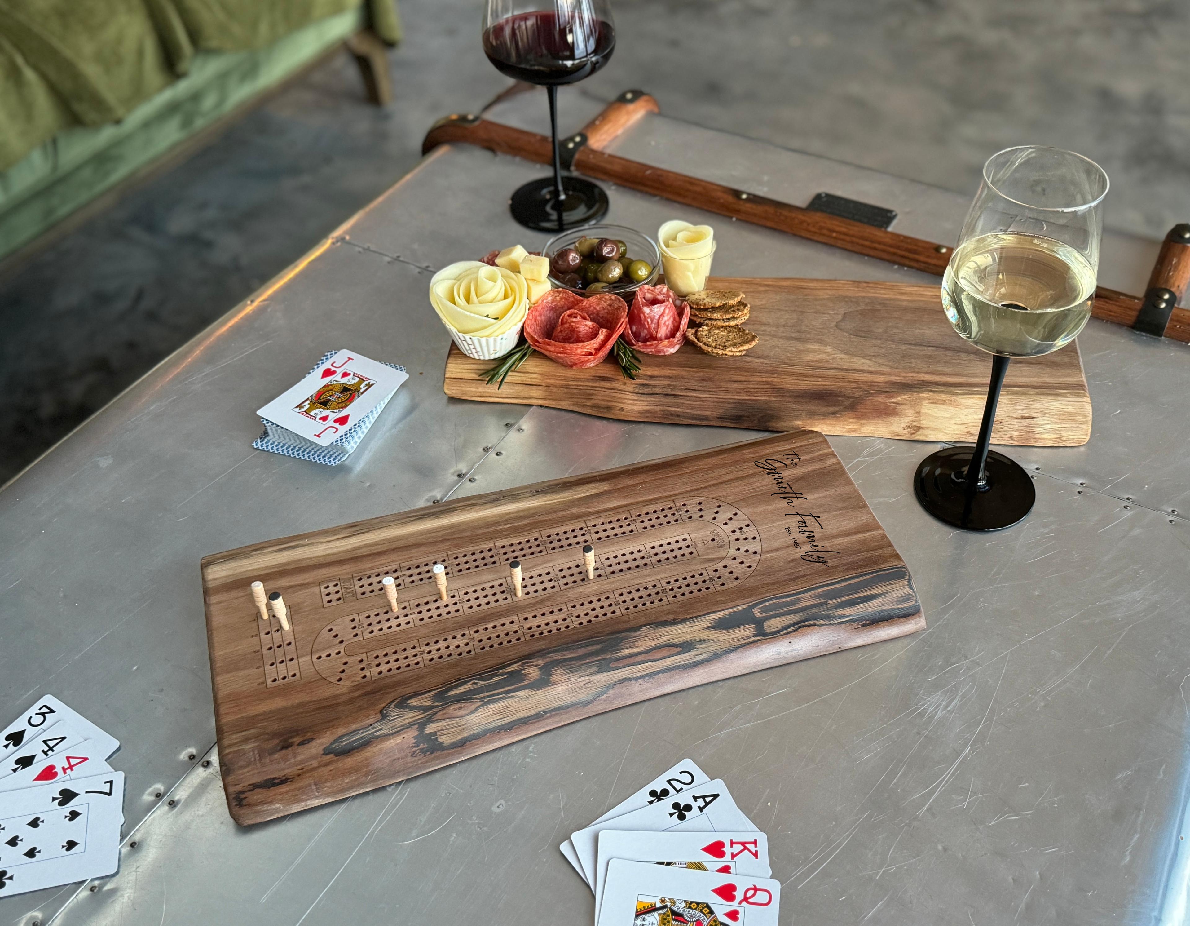 Personalized Live Edge Cribbage Board with pegs and cards on a table with a live edge charcuterie board and a couple glasses of wine.