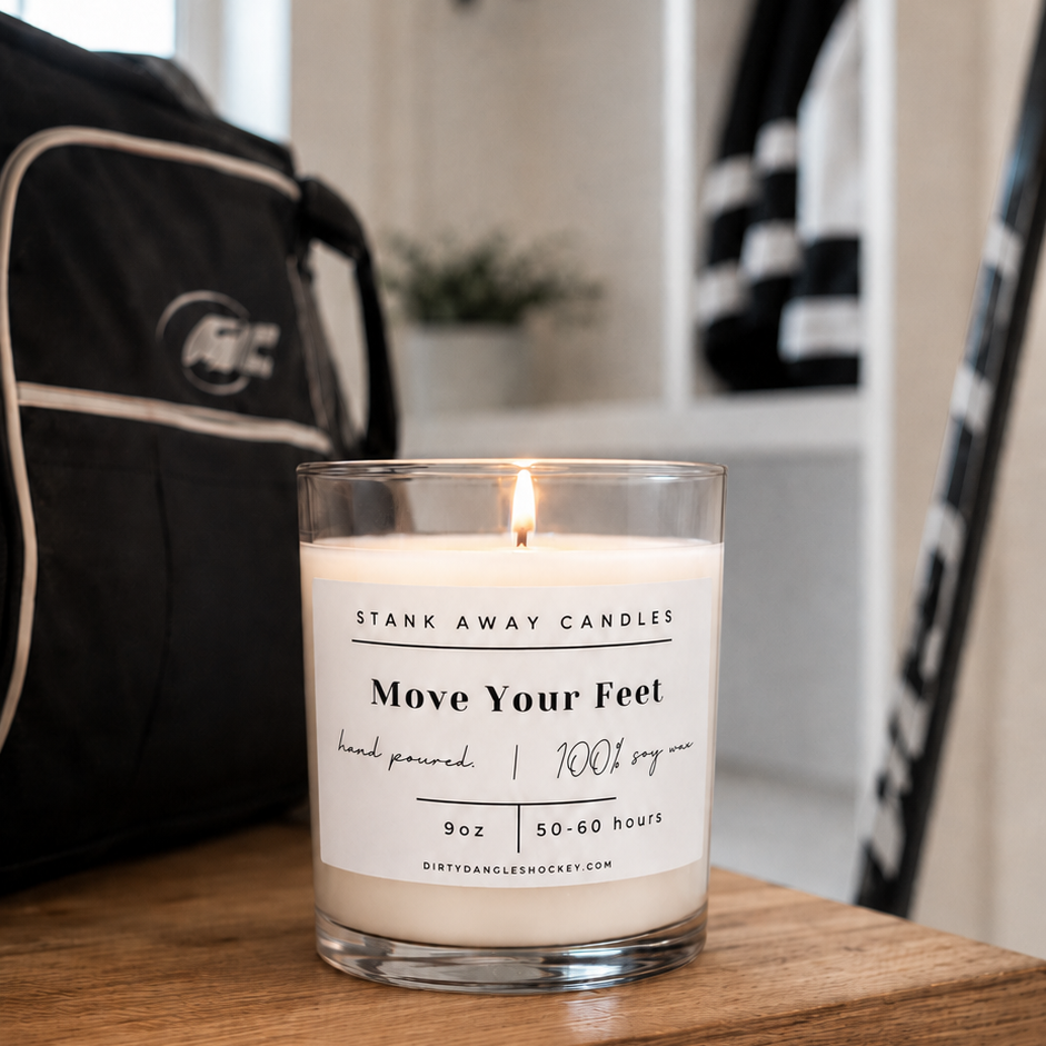 A white scented hockey candle on a wooden bench with hockey gear. Move Your Feet
