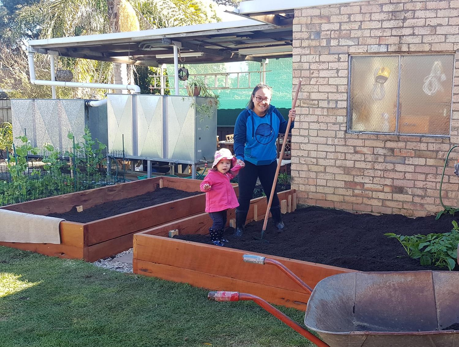 Woman and young child standing in newly filled raised garden beds beside a house.