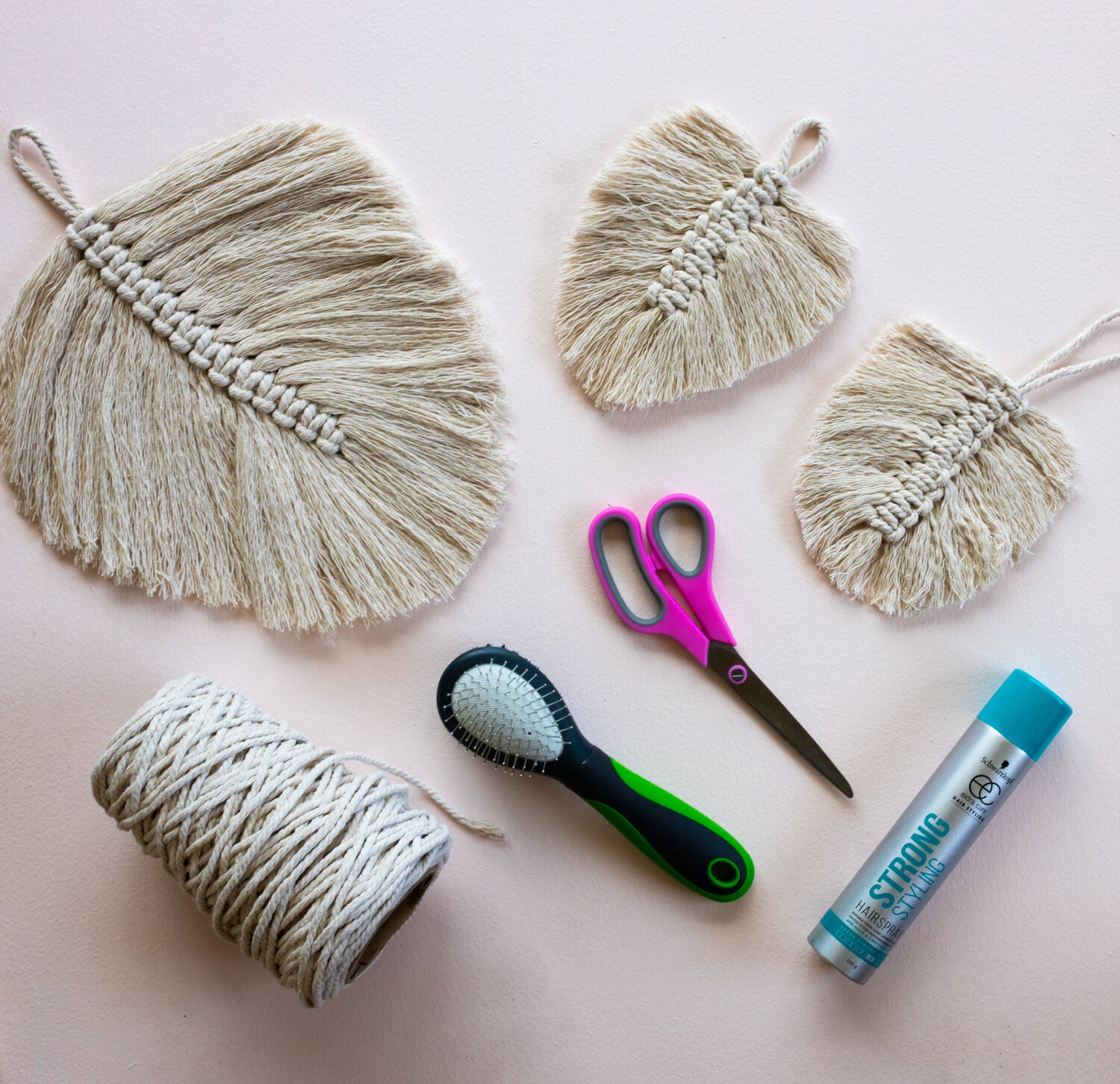Finished macrame leaves and supplies for the project lie on a table - scissors, macrame string, a hairbrush, and hairspray.