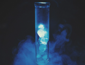 Bong mouthpiece against a black background, filled with ice and surrounded in blue light and smoke
