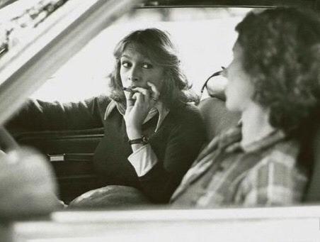 Black and white photo of Laurie Strode and Annie sharing a joint in the car from Halloween (1978), demonstrating how distraction equals death for stoners in classic slasher horror movies.