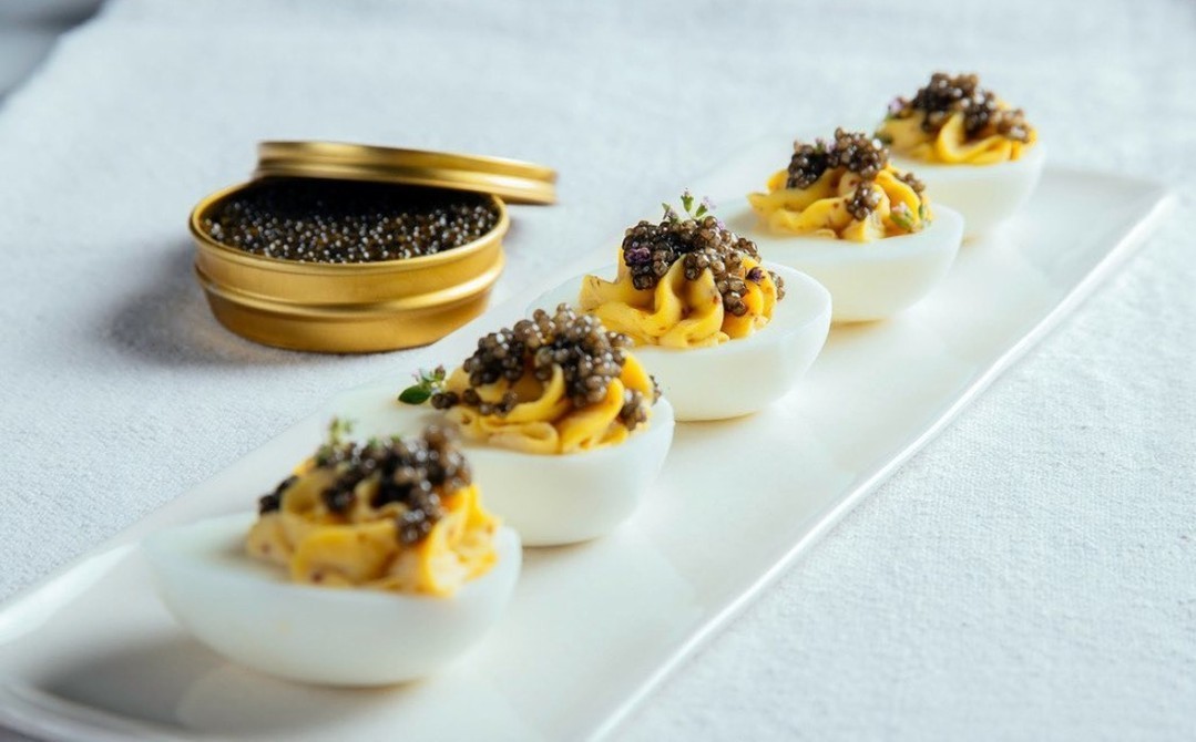 An opened caviar tin and deviled eggs dish