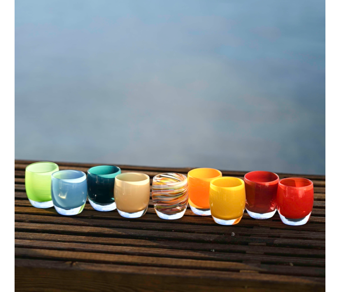 glassybaby transparent glass votive holders in oranges, reds and yellows on wooden bench