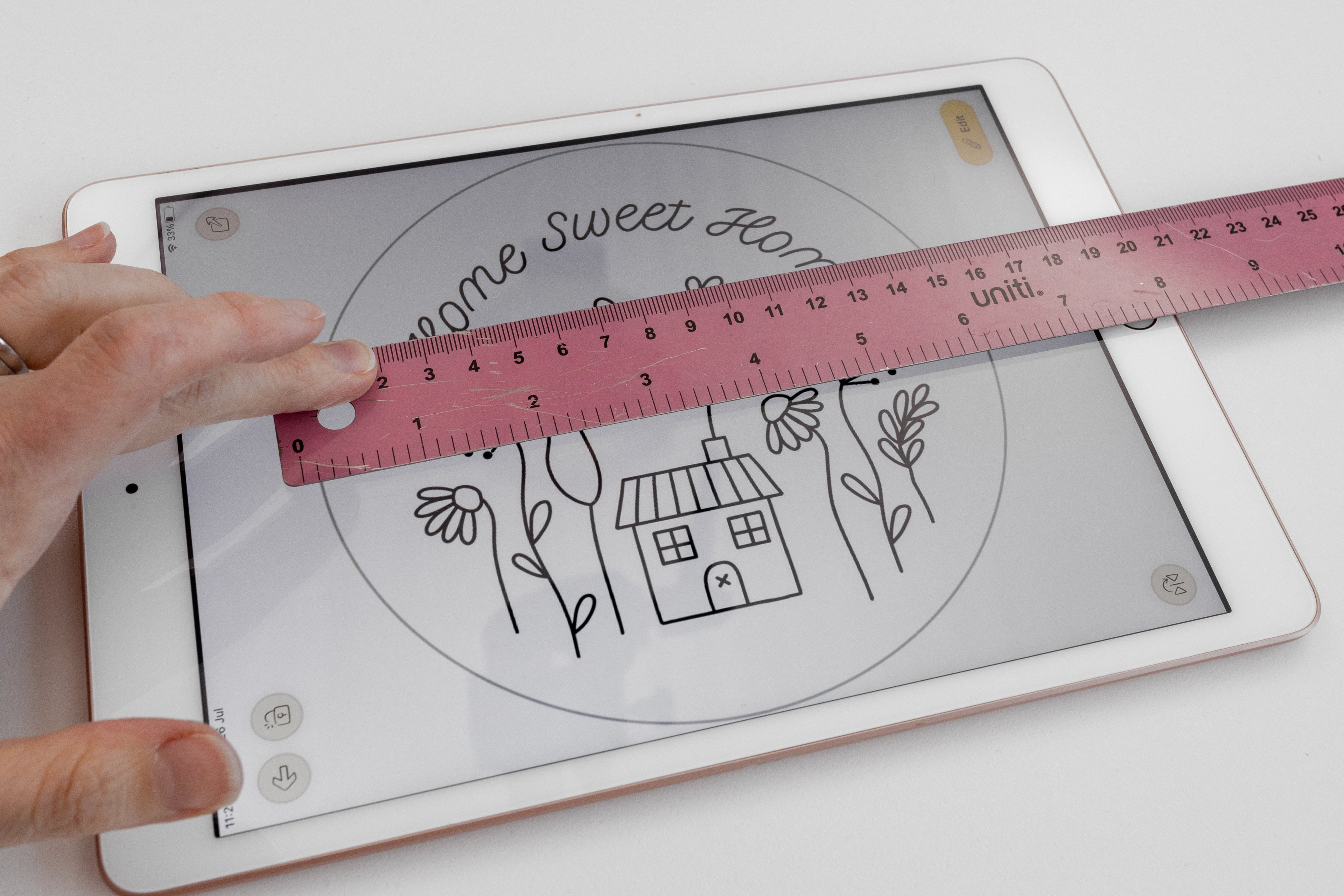 A hand holds a ruler over an ipad with a pattern on it.