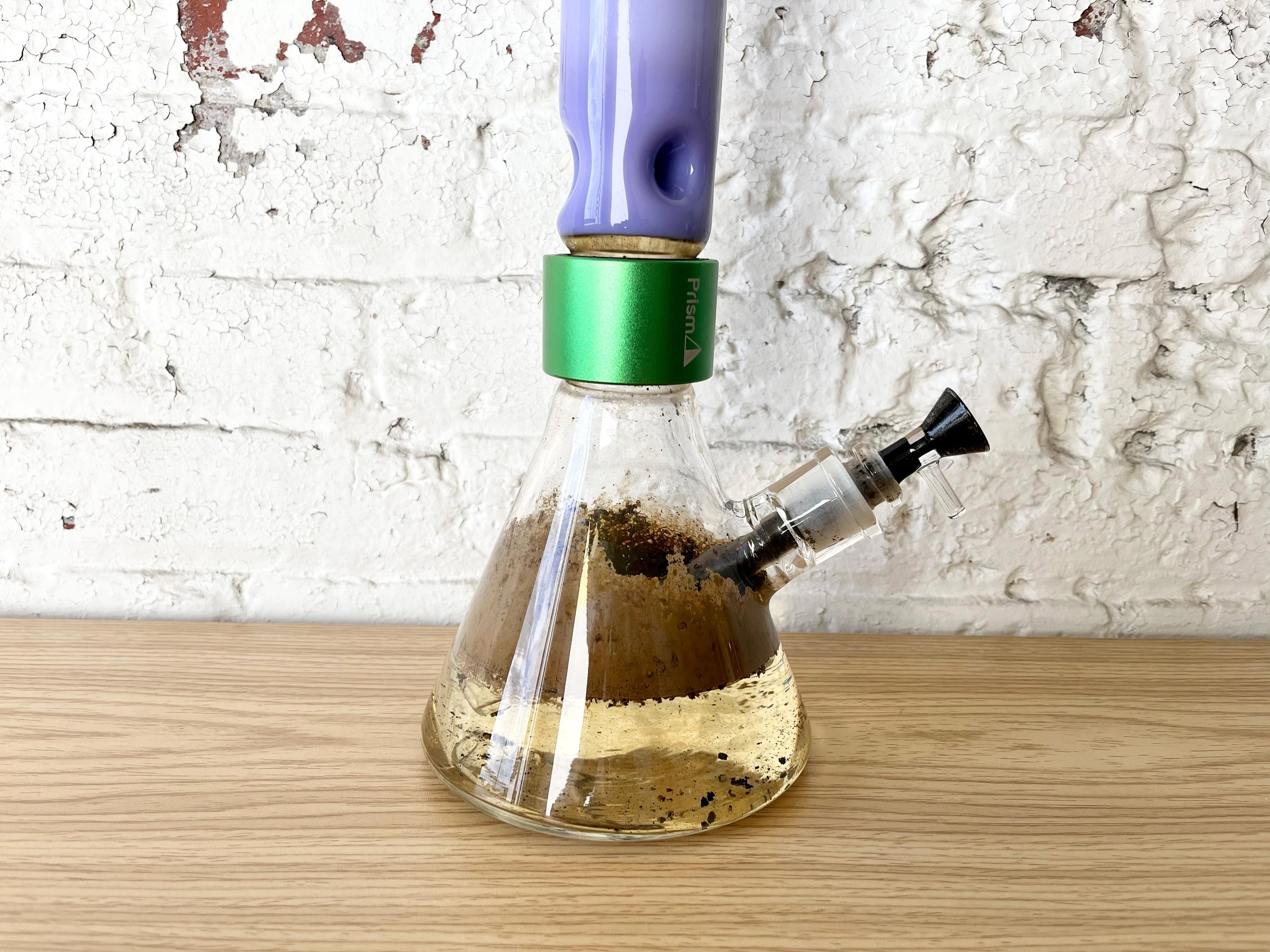 "A macro close-up of a Prism beaker bong base filled with stagnant, dirty water and dark resin buildup. This detailed shot illustrates the risk of mold and bacteria growth in glass water pipes when not cleaned every 24 to 48 hours, highlighting the importance of the modular design for easy maintenance and a cleaner smoking experience."