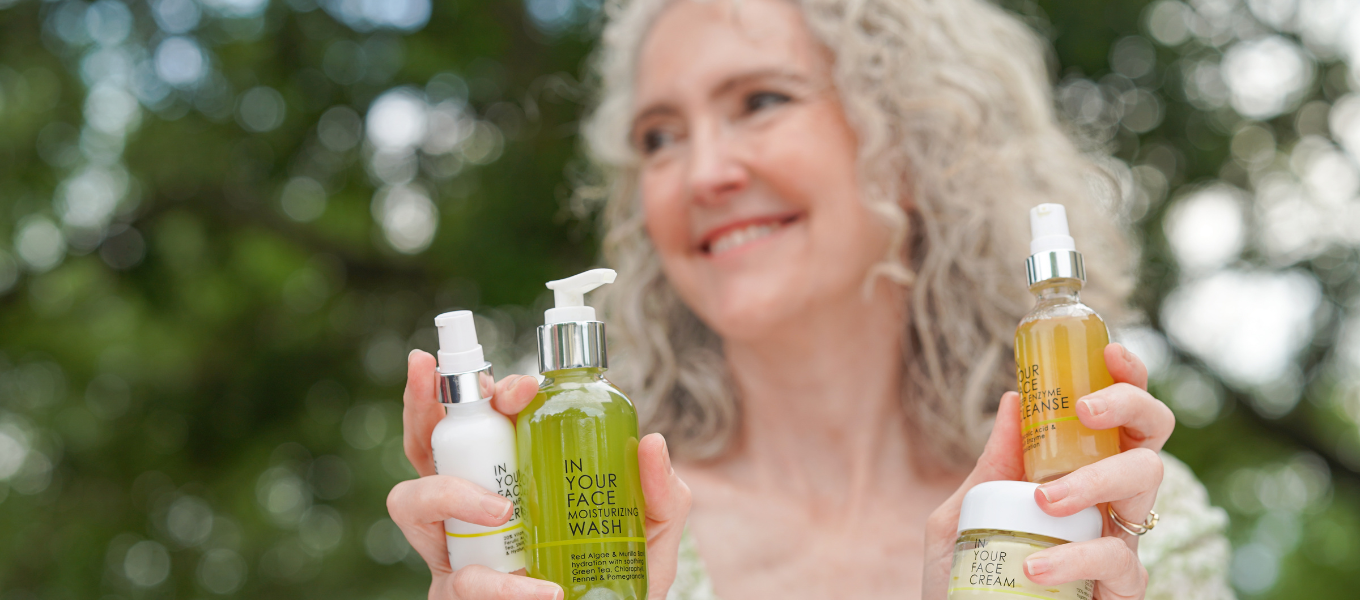 IN YOUR FACE REWARDS, a pretty mature woman holding 4 IN YOUR FACE products on a green leafy background