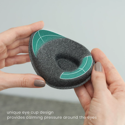 Hands holding one tapered eye cup of a weighted eye mask for sleep. The cup has an indentation.
