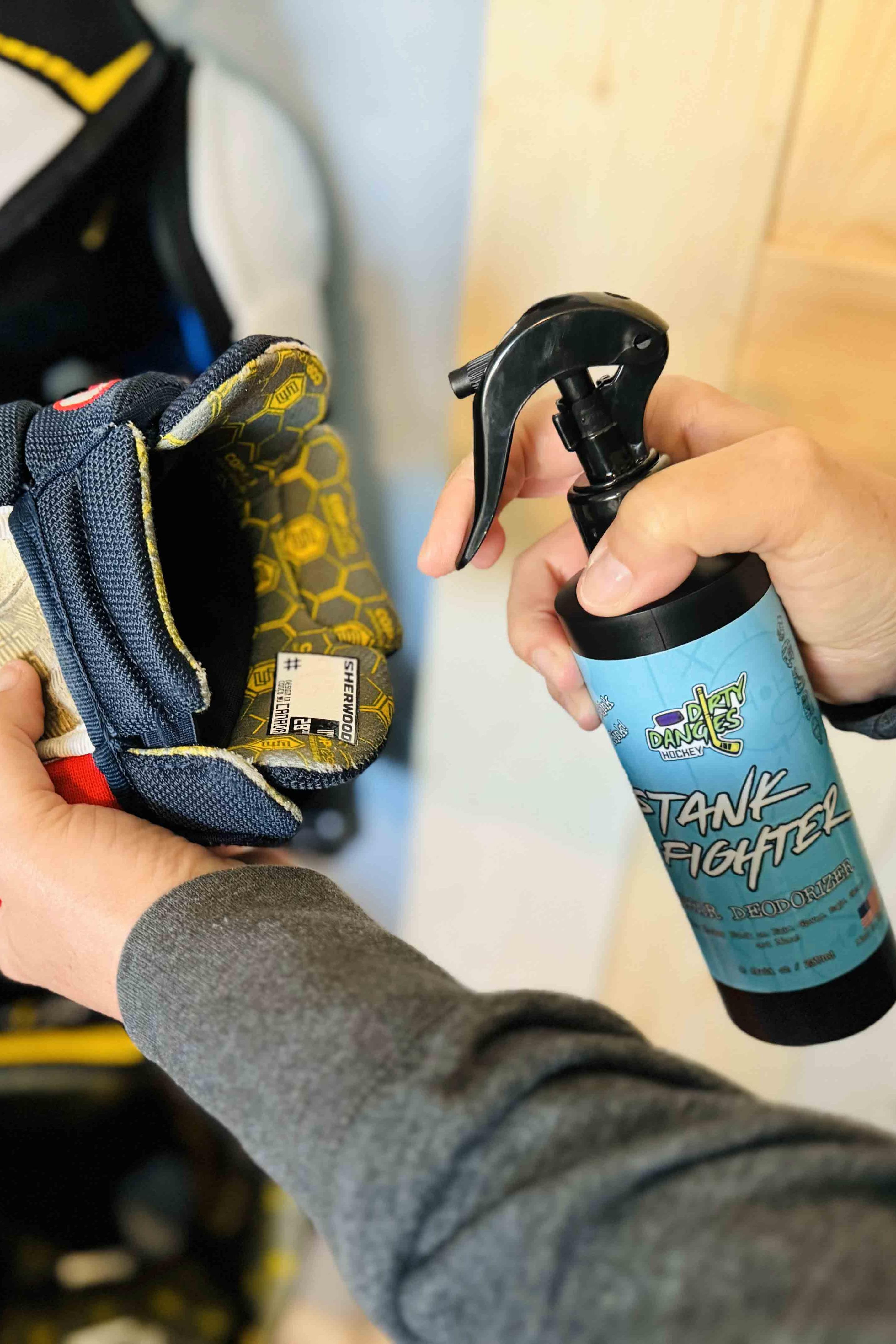 A hockey mom spraying stank fighter hockey gear deodorizer into a red white and blue hockey glove