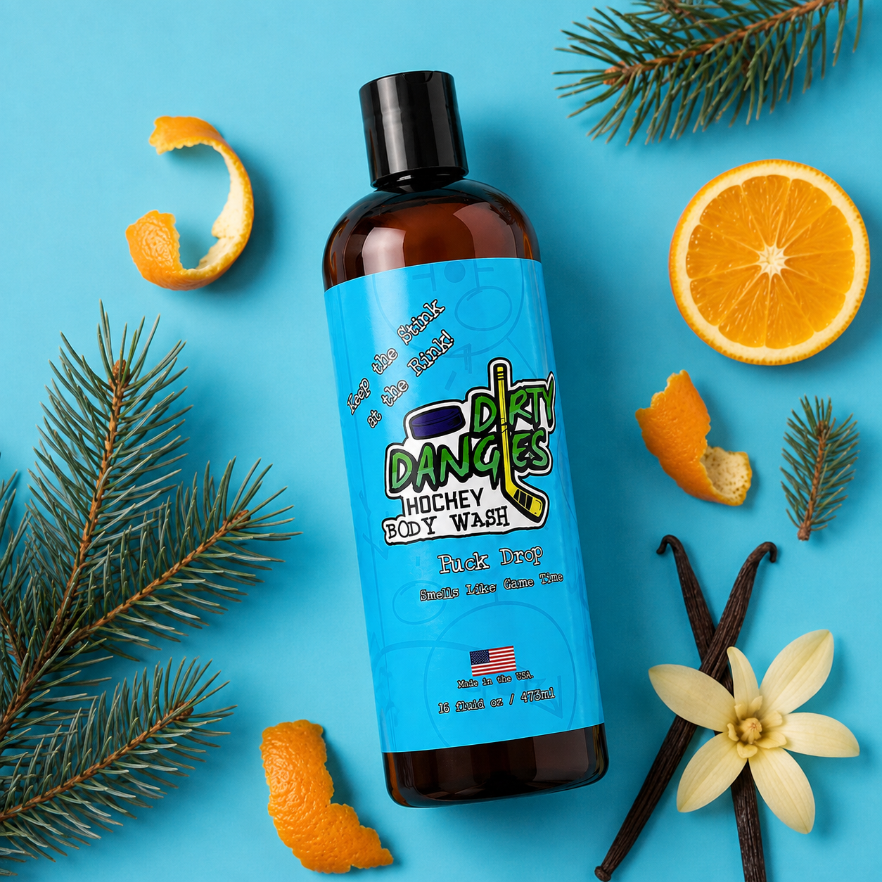 a bottle of puck drop orange, pine and vanilla scented hockey body wash on a blue background with pine needles, orange peels and vanilla.