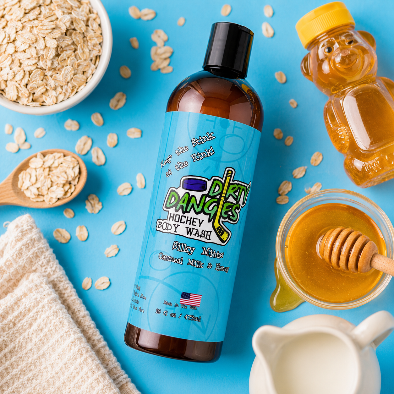 a bottle of silky mitts oatmeal milk and honey scented hockey body wash on a blue background with oats, oatmilk and honey.