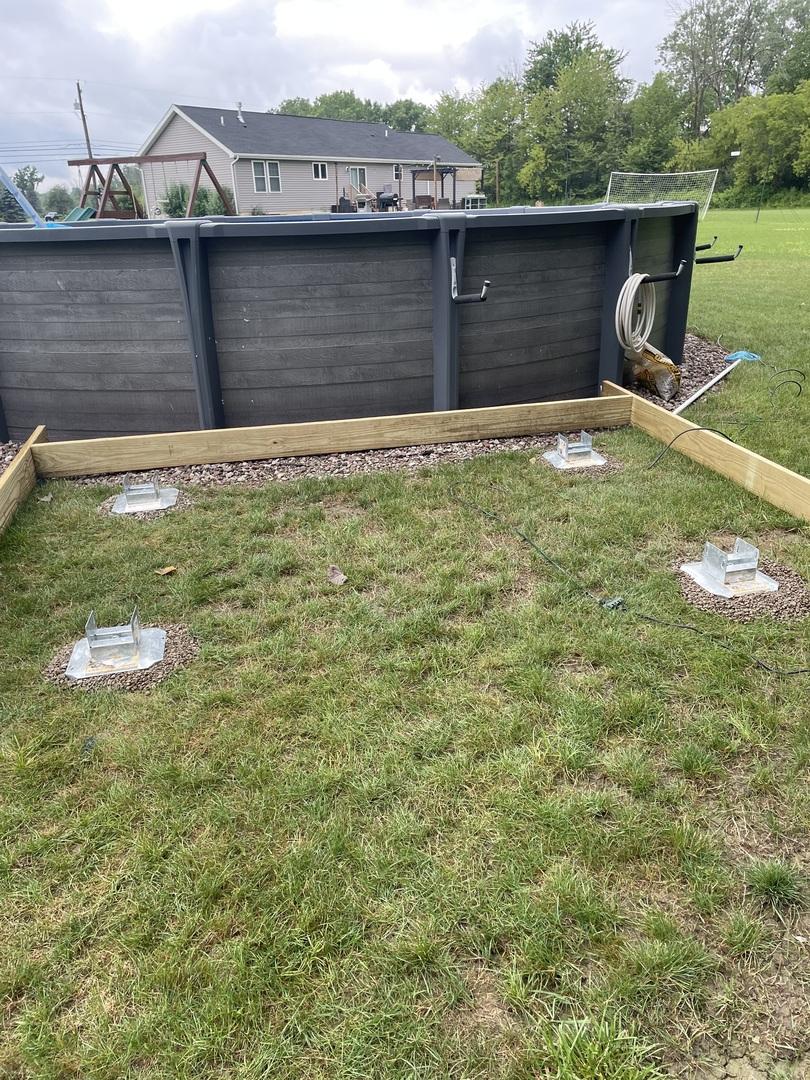 deck foot anchors installed directly into the ground beside a dark grey pool