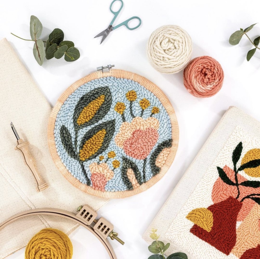 This image shows a Brilliant Botanicals punch needle pattern surrounded by punch needle supplies.