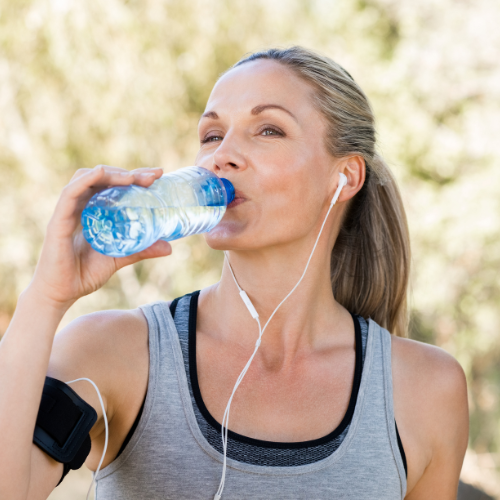 active woman wearing headphones and drinking out of a plastic water bottle
