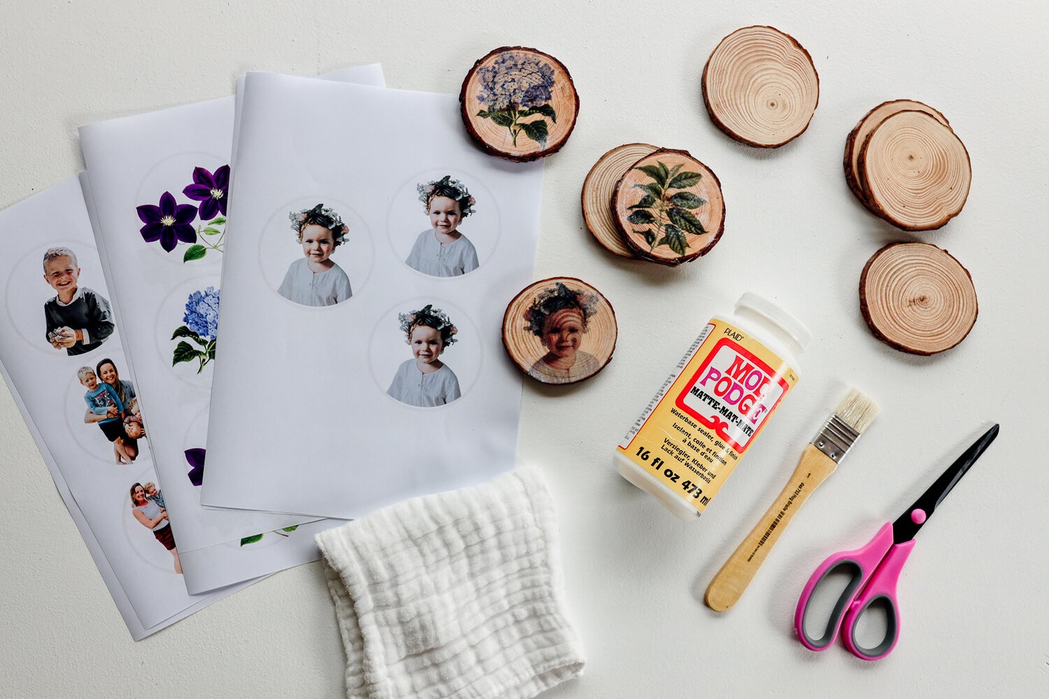 Supplies are lying on a table - printed photos, wood, Mod Podge, brush, scissors, and cloth.
