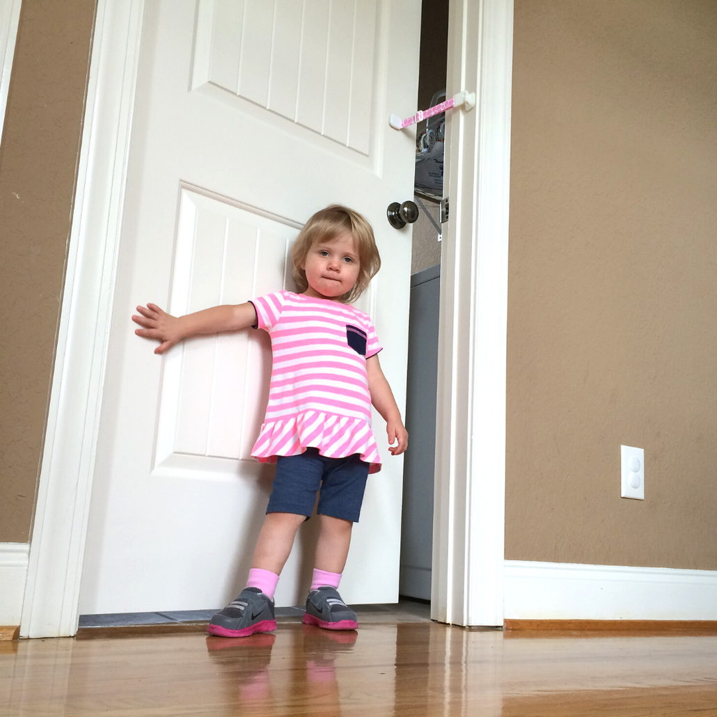 Toddler opening a door in a home, illustrating the need for Door Buddy baby proof door strap solutions.