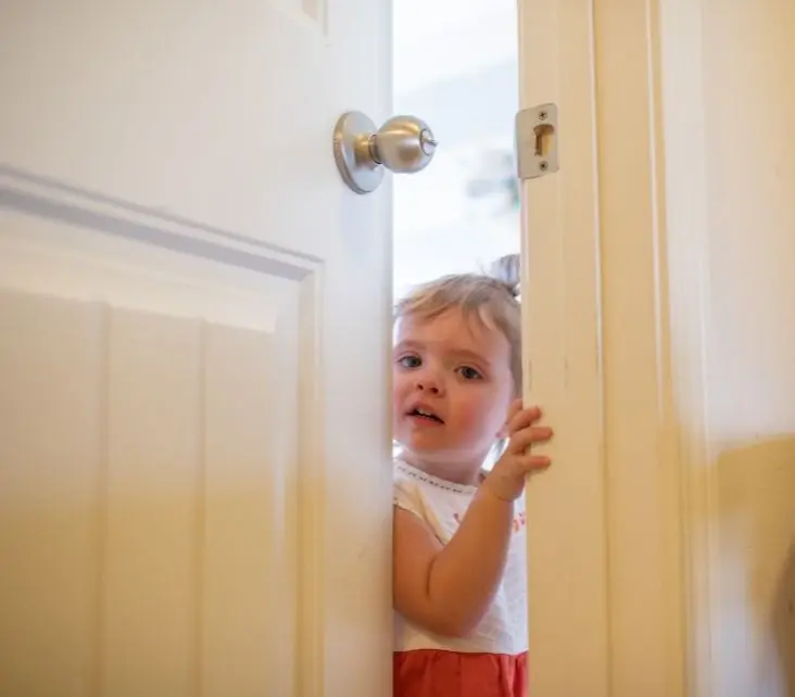 A young boy stretches his arm to grasp the handle of a door, showing curiosity and eagerness to enter.