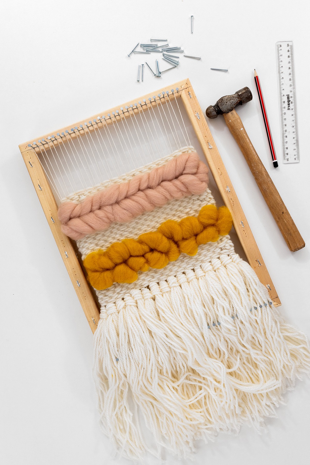 This image shows a DIY frame loom with all the supplies around it.