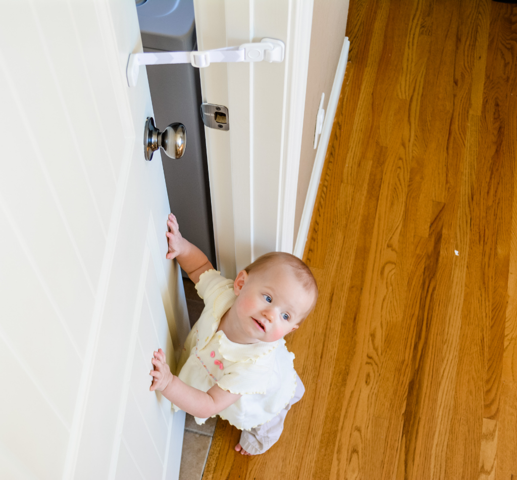 A baby looks up at a partially open door held in place by The Door Buddy door strap. The adjustable strap keeps the door open just enough for cats to pass through while helping prevent babies and toddlers from entering the room.