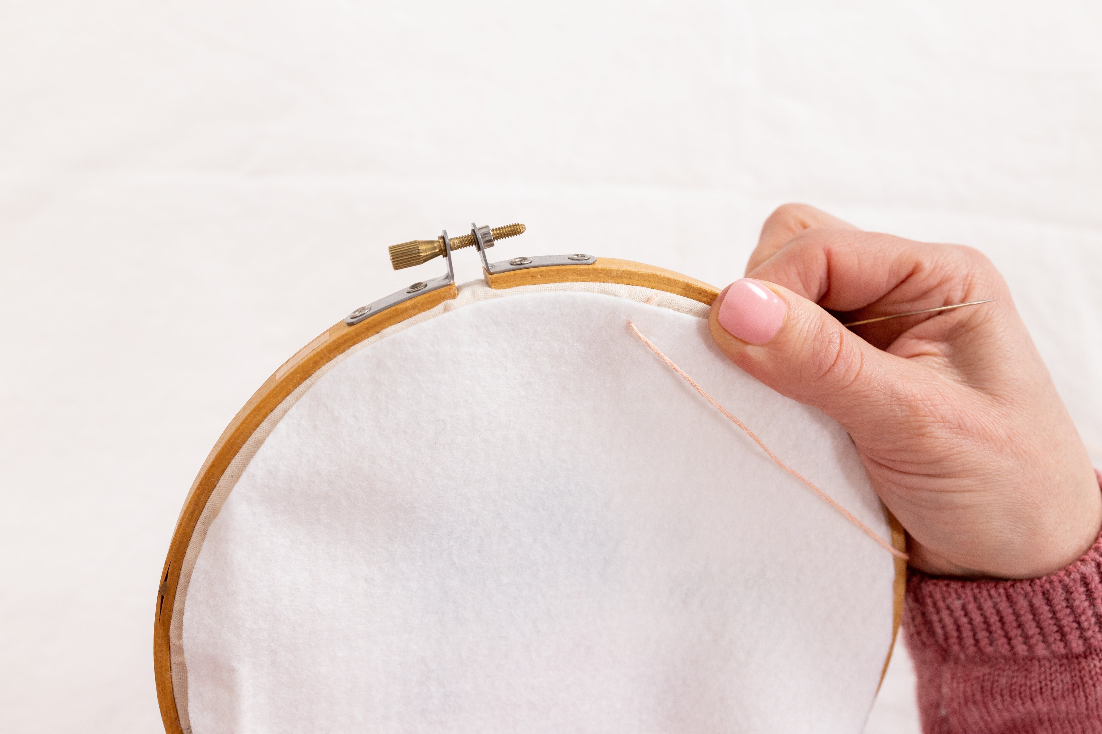 A hand holds a piece of fabric on the back of the hoop and a needle is pulled up through the back.