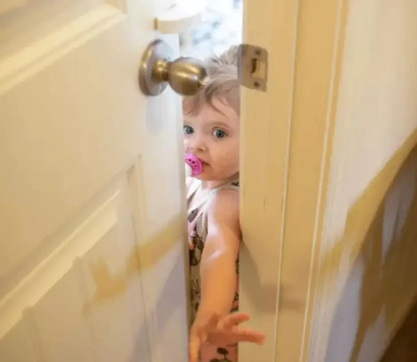 Toddler reaching up and trying to open a closed door with a childproof handle cover, showing a barrier used to keep a toddler out of restricted areas like a room with a litter box.