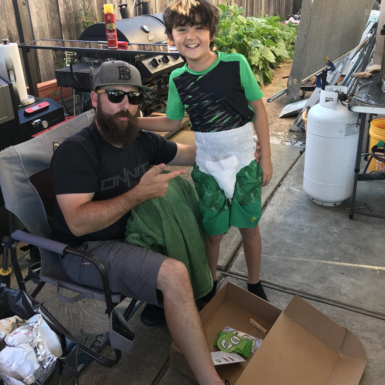 A man smiling and pointing to his kid wearing an adult diaper from the deluxe dutch oven kit.