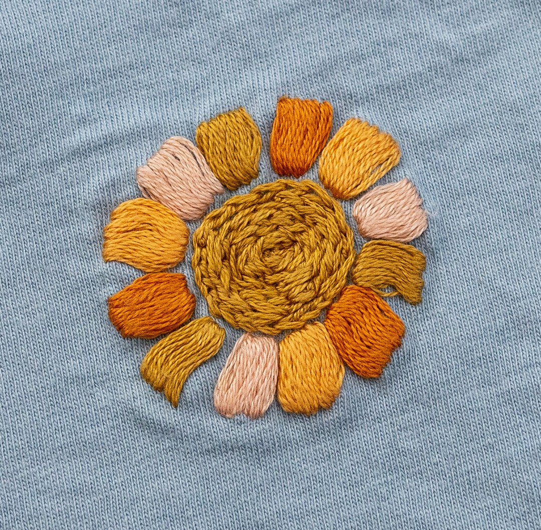 An embroidered sun is stitched in fabric.