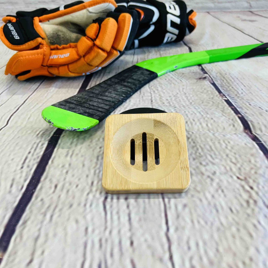 A bamboo soap dish on a wood background with a hockey stick and a hockey glove.