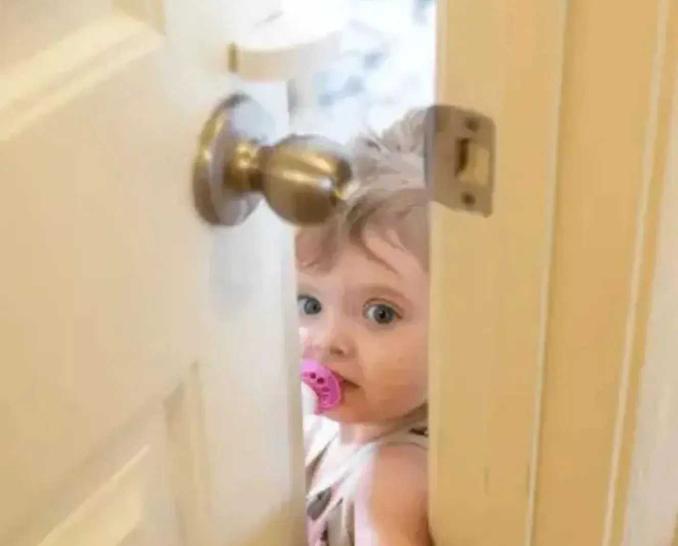 A curious baby peeks through a house door, highlighting the importance of keeping children away from the litter box.