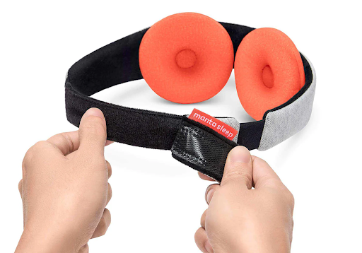 Hands holding the micro hook and loop closure of a warm compression eye mask with orange eye cups.