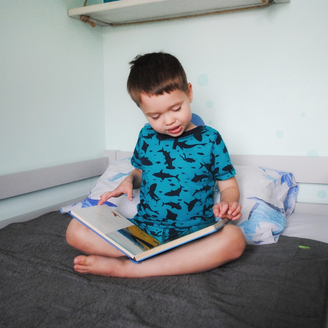 boy reading a book sitting on the bed protected with waterproof bed mat PeapodMat