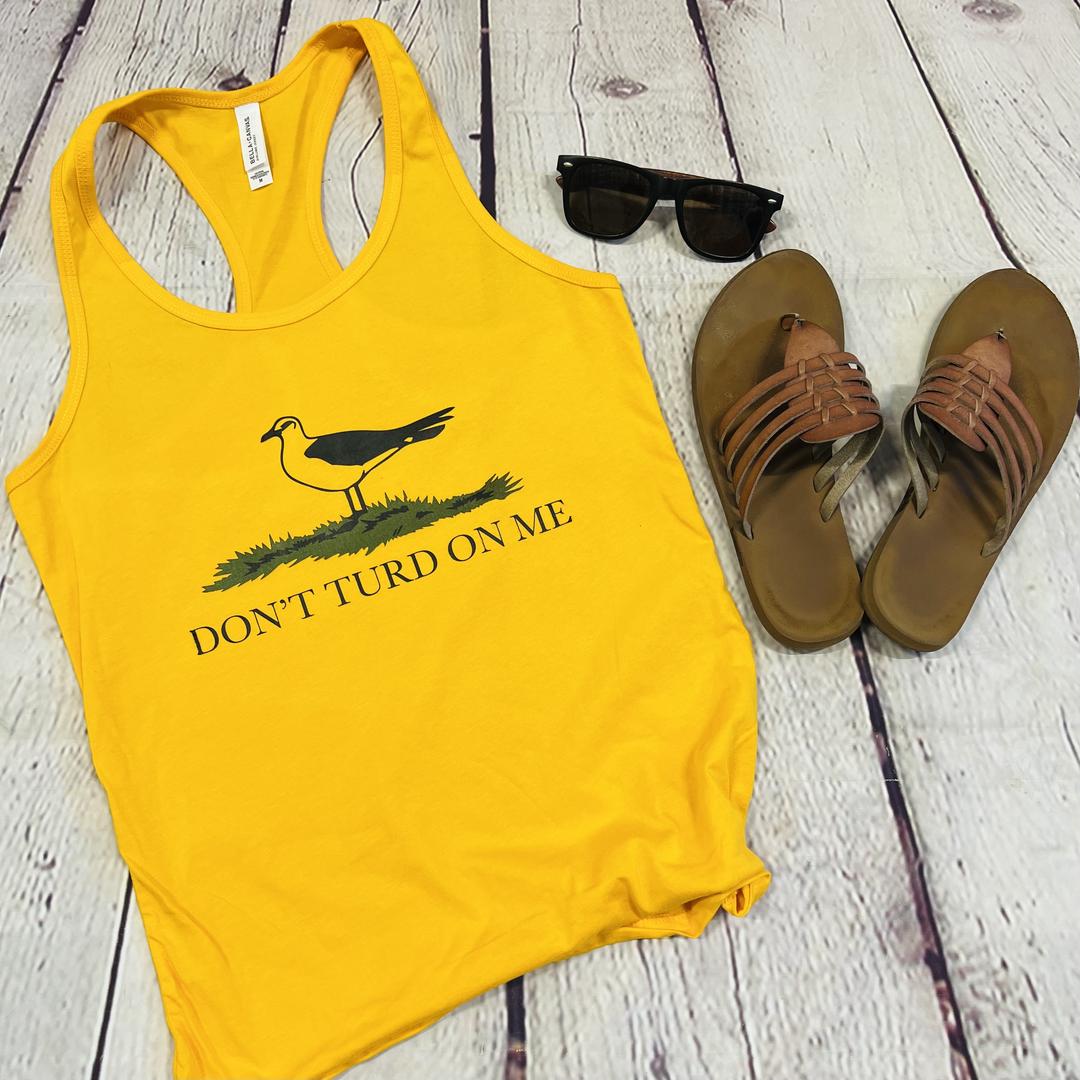 Picture of a gold and yellow women's tank top with a picture of a seagull standing in the grass. Text on the women's tank top says "Don't Turd On Me." Similar to the Gadsden "Dont Tread On Me" Flag