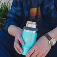 A man holding a blue dirty dangles 2 in 1 drink tumbler can cooler outside.