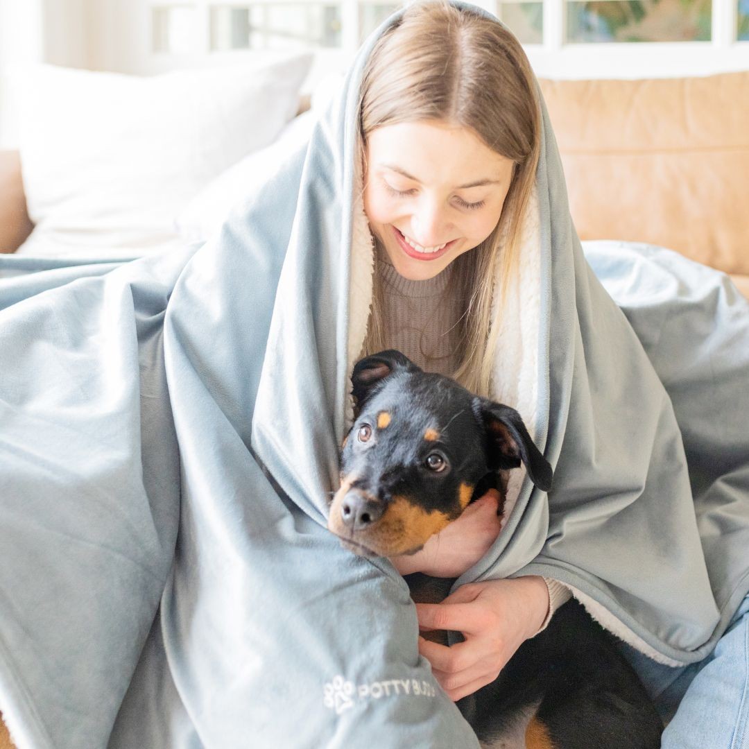 Girl sitting on sofa with rottweiler puppy, blanket around shoulders