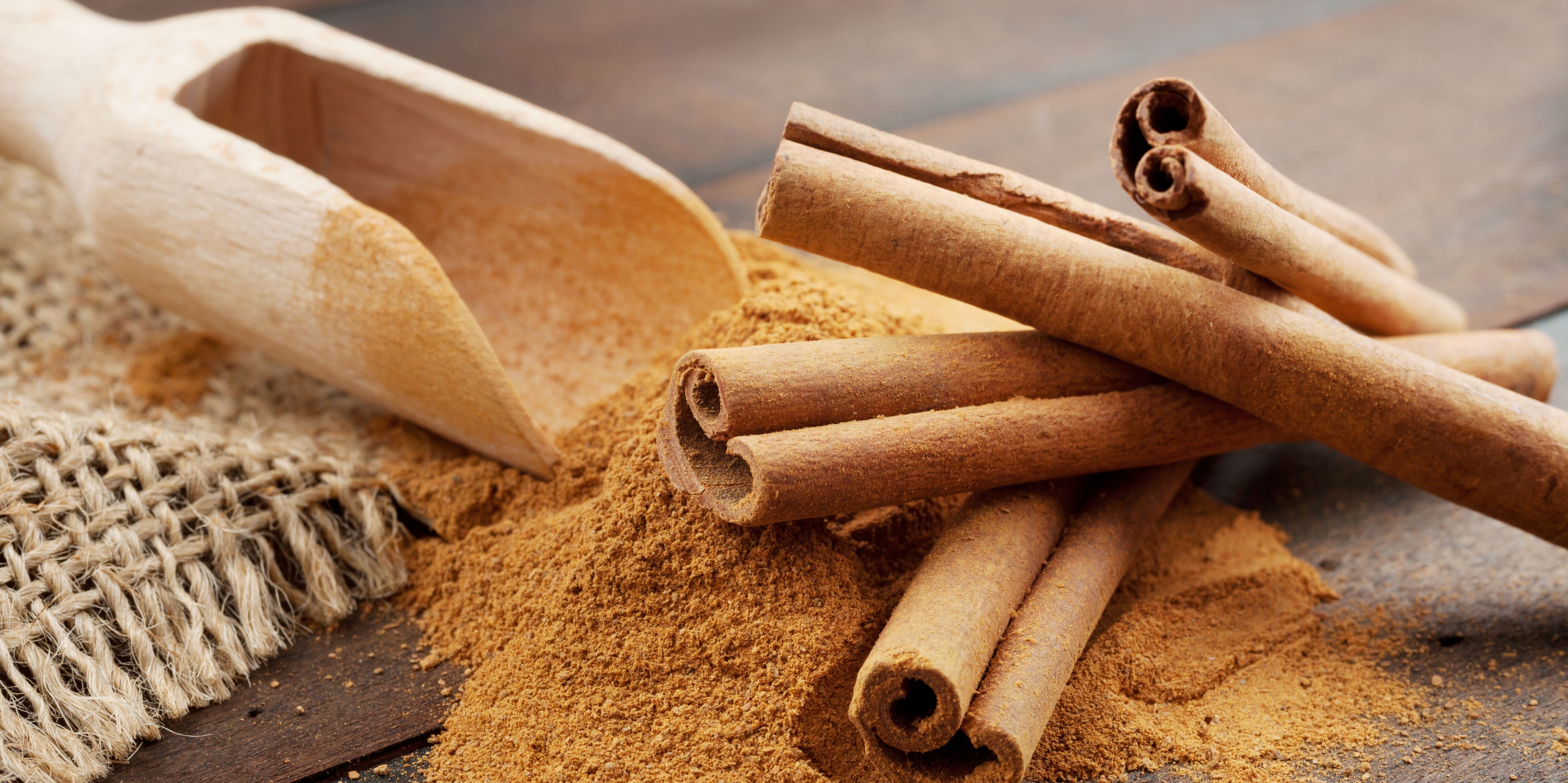 Stacked cinnamon stick on top of cinnamon powder with a wooden scoop