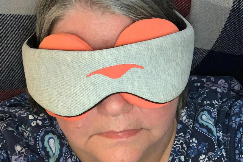 A woman wearing a gray sleep mask with orange warming eye cups.